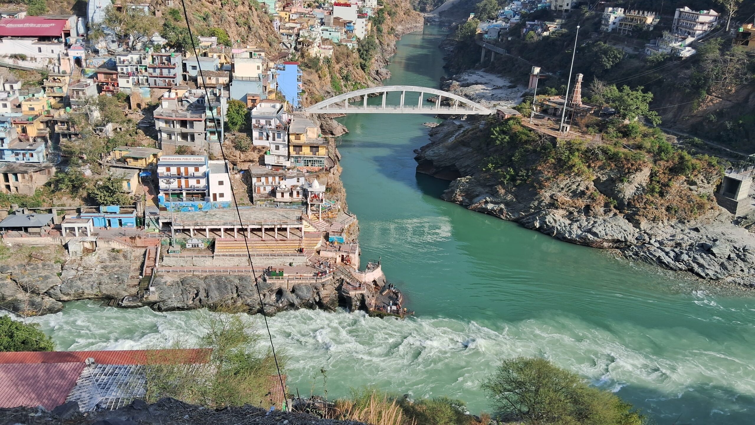 Confluence of rivers Alaknanda and Bhagirathi at Devprayag with a bridge and colorful houses in Uttarakhand